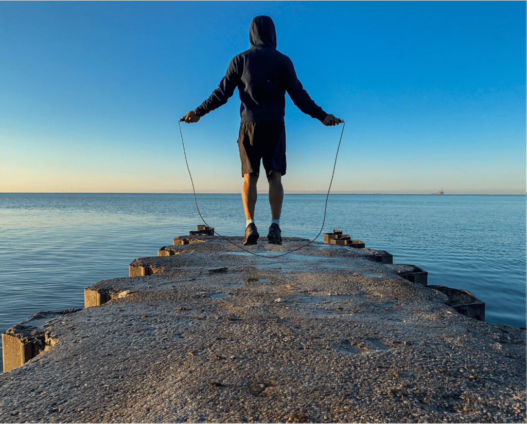 Man skipping rope alone on a pier at sunrise